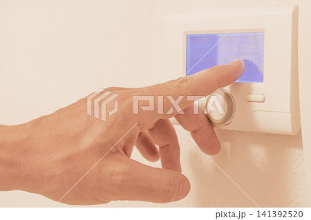 Male hand pointing finger at digital screen of smart home thermostat panel showing indoor outdoor temperature data for heating control and energy saving Male hand pointing finger at digital screen of smart home thermostat panel showing indoor outdoor temperature data for heating control and energy saving 141392520
