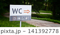 Sign directs visitors to restrooms in a park setting near a path 141392778