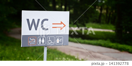 Sign directs visitors to restrooms in a park setting near a path Sign directs visitors to restrooms in a park setting near a path 141392778