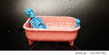 Blue skeleton toy in a pink bathtub with water on a black background Blue skeleton toy in a pink bathtub with water on a black background 141392782