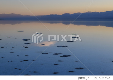 Peaceful sunset reflection on shallow water with mountain range silhouette of sierra nevada usa bringing serene tranquil mood to empty vast beautiful natural landscape environment Peaceful sunset reflection on shallow water with mountain range silhouette of sierra nevada usa bringing serene tranquil mood to empty vast beautiful natural landscape environment 141394692
