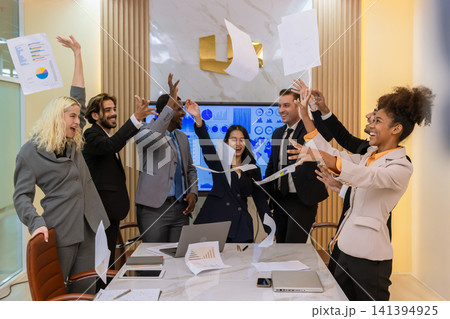 A multi-ethnic professional team celebrating a project completion by tossing papers in the air at a modern boardroom, expressing joy, teamwork, and corporate achievement. A multi-ethnic professional team celebrating a project completion by tossing papers in the air at a modern boardroom, expressing joy, teamwork, and corporate achievement. 141394925