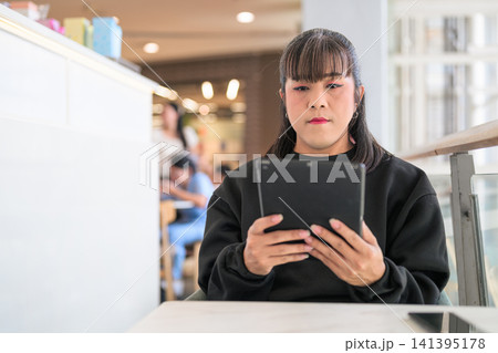 Thai Transgender Woman Reading on Digital Tablet Indoors Thai Transgender Woman Reading on Digital Tablet Indoors 141395178