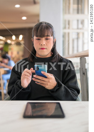 Thai Transgender Woman Texting on Smartphone with Tablet on Table 141395180
