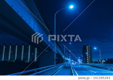 青い光に包まれた夜の橋と高架橋、遠くに輝くマンション群の都市風景 141395263