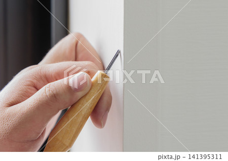白いドア枠の補修箇所にキリで印をつける職人の手元の接写 白いドア枠の補修箇所にキリで印をつける職人の手元の接写 141395311