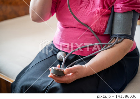 Person wearing an arm blood pressure monitor at home on a sofa. Cardiovascular health and hypertension management through self monitoring Person wearing an arm blood pressure monitor at home on a sofa. Cardiovascular health and hypertension management through self monitoring 141396036