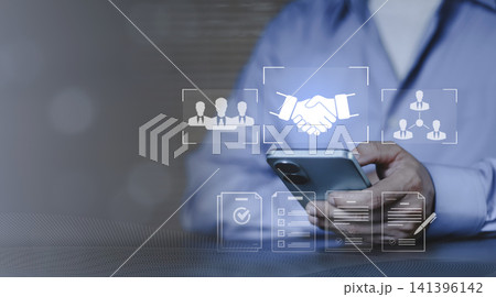 Concept of partnership agreement, professional CRM and human resources coordination. Hand using smartphone with icons for business handshake deal, procurement, team management and verified documents Concept of partnership agreement, professional CRM and human resources coordination. Hand using smartphone with icons for business handshake deal, procurement, team management and verified documents 141396142