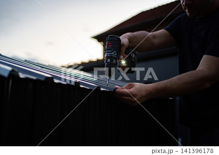 Man drilling screw into metal roof with cordless screwdriver Man drilling screw into metal roof with cordless screwdriver 141396178