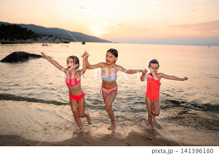 Children holding hands running into ocean at sunset Children holding hands running into ocean at sunset 141396180