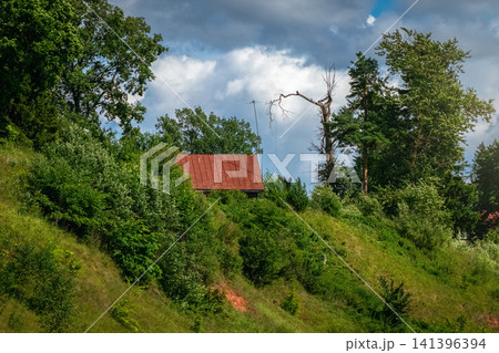 Rustic log cabin with red metal roof on green grassy hill slope under dramatic sky Rustic log cabin with red metal roof on green grassy hill slope under dramatic sky 141396394
