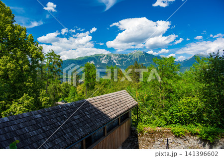 Scenic view of the wooden footbridge near Bled Castle on Lake Bled, Slovenia, with the majestic Julian Alps rising in the background on a clear summer day. Scenic view of the wooden footbridge near Bled Castle on Lake Bled, Slovenia, with the majestic Julian Alps rising in the background on a clear summer day. 141396602