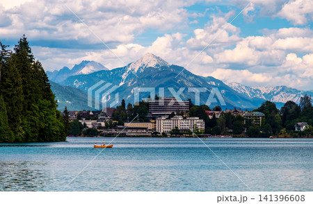 Small rowing boat with two unrecognizable people sailing across Lake Bled in Slovenia, with the town of Bled and the majestic Julian Alps rising in the background. Small rowing boat with two unrecognizable people sailing across Lake Bled in Slovenia, with the town of Bled and the majestic Julian Alps rising in the background. 141396608