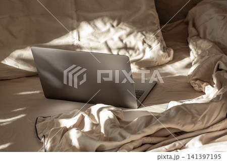 Laptop on a cozy bed getting morning sunlight Laptop on a cozy bed getting morning sunlight 141397195