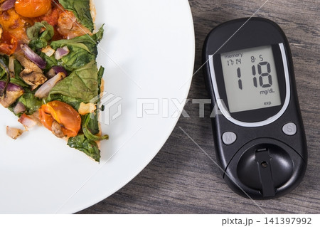 Glucose meter with result of sugar level and fresh baked vegetarian pizza. Nutrition during diabetes 141397992