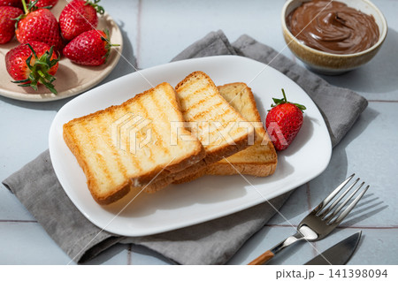 Toasted bread, chocolate cream and strawberry on a plate on a blue tile background Toasted bread, chocolate cream and strawberry on a plate on a blue tile background 141398094