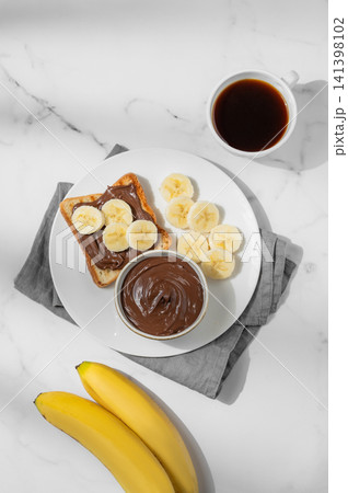 Toasted bread with chocolate cream and banana on a plate on a marble background Toasted bread with chocolate cream and banana on a plate on a marble background 141398102