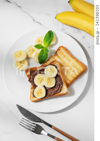 Toasted bread with chocolate cream and banana on a plate on a marble background Toasted bread with chocolate cream and banana on a plate on a marble background 141398103