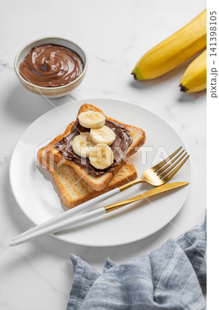 Toasted bread with chocolate cream and banana on a plate on a marble background Toasted bread with chocolate cream and banana on a plate on a marble background 141398105