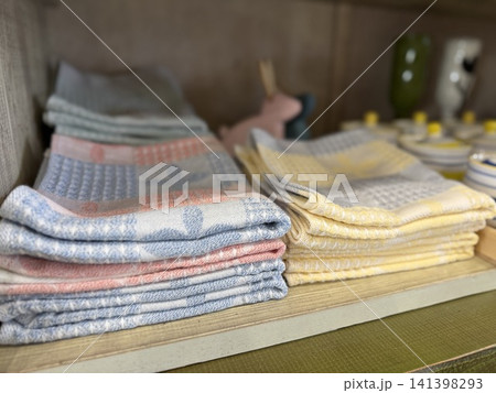 Folded kitchen towels in soft pastel colors neatly stacked on a shelf background 141398293