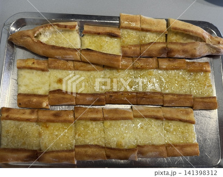 Turkish pide with melted cheese served on a metal tray, traditional flatbread presentation Turkish pide with melted cheese served on a metal tray, traditional flatbread presentation 141398312