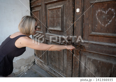 Woman tries to pull open heavy weathered wooden doors with antique iron handles in historic setting. Curiosity, heritage architecture, effort, tradition, vintage entrance, exploration, travel Woman tries to pull open heavy weathered wooden doors with antique iron handles in historic setting. Curiosity, heritage architecture, effort, tradition, vintage entrance, exploration, travel 141398935