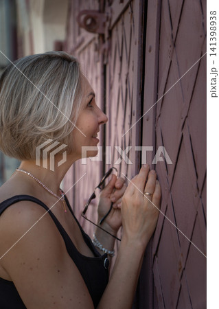 Woman peeks through narrow gap in historic red wooden door while exploring old Moscow street. Curiosity, mystery, heritage architecture, discovery, travel, urban lifestyle, authentic atmosphere 141398938
