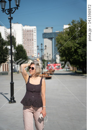 Woman cools off beneath bright summer sun on Shkolnaya Street in Moscow while carrying drinking water. Hydration, urban lifestyle, travel, wellbeing, heat, city exploration, leisure Woman cools off beneath bright summer sun on Shkolnaya Street in Moscow while carrying drinking water. Hydration, urban lifestyle, travel, wellbeing, heat, city exploration, leisure 141398972