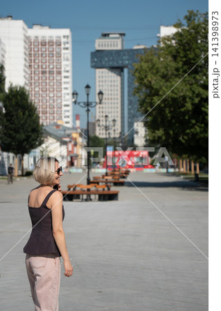 Smiling woman talks on smartphone while walking along Shkolnaya Street in Moscow on sunny summer day. Urban lifestyle, mobile communication, city travel, freedom, modern living, outdoor leisure Smiling woman talks on smartphone while walking along Shkolnaya Street in Moscow on sunny summer day. Urban lifestyle, mobile communication, city travel, freedom, modern living, outdoor leisure 141398973