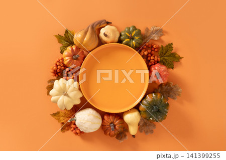 Orange plate framed by pumpkins and autumn leaves flat lay 141399255