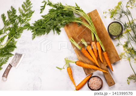 Fresh raw carrots with greens on cutting board Fresh raw carrots with greens on cutting board 141399570