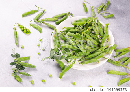 Fresh green pea pods on white plate and scattered on background 141399578