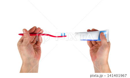 two hands holding a red toothbrush and a tube of paste on a white background 141401967