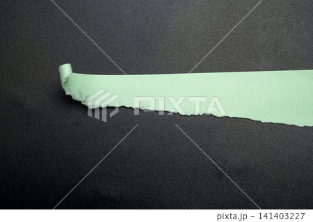A piece of torn light green paper with a curled edge on a dark textured background 141403227