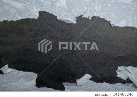 A close-up shot of white paper torn horizontally, revealing a deep black, gritty, and textured background. Concept of mystery, hidden truth, or reveal 141403240