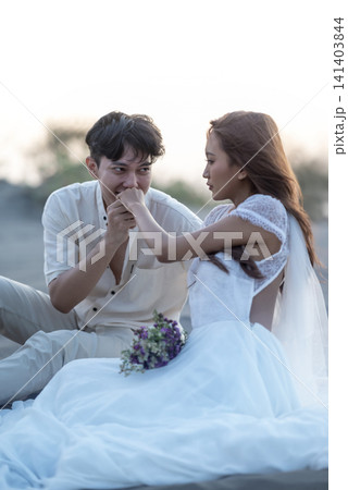 A Indonesian southeast asian romantic couple in white clothes shares an intimate moment as the man kisses the woman's hand on a sandy beach during beautiful sunset, capturing their love and engagement A Indonesian southeast asian romantic couple in white clothes shares an intimate moment as the man kisses the woman's hand on a sandy beach during beautiful sunset, capturing their love and engagement 141403844