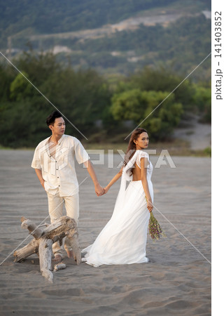 A joyful young Indonesian southeast asian wedding couple holding hands and walking together on a sandy beach during sunset A joyful young Indonesian southeast asian wedding couple holding hands and walking together on a sandy beach during sunset 141403852