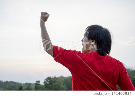An enthusiastic Indonesian man wearing a red t-shirt and traditional red and white headband cheering with a fist raised in the air. Hari Kemerdekaan Dirgahayu Indonesia An enthusiastic Indonesian man wearing a red t-shirt and traditional red and white headband cheering with a fist raised in the air. Hari Kemerdekaan Dirgahayu Indonesia 141403934