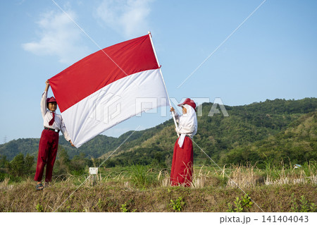 Two Indonesian school children in uniform proudly holding the red and white Indonesian national flag, celebrating national pride. Hari Kemerdekaan, Merdeka, and Dirgahayu Indonesia on 17 Agustus Two Indonesian school children in uniform proudly holding the red and white Indonesian national flag, celebrating national pride. Hari Kemerdekaan, Merdeka, and Dirgahayu Indonesia on 17 Agustus 141404043