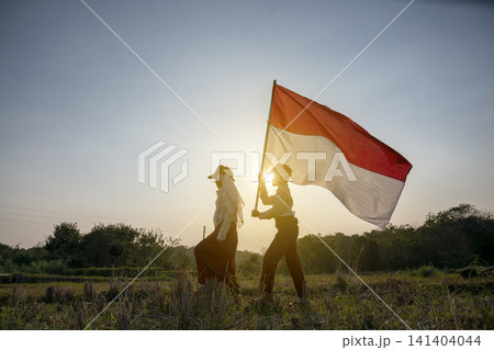 Silhouette of two young Indonesian students walking at sunset, with one student holding and waving the Indonesian national flag. Hari Kemerdekaan, Merdeka, and Dirgahayu Indonesia on 17 Agustus 141404044