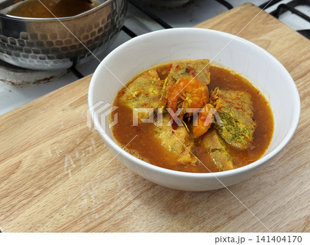 Homemade Thai sour curry with shrimp and fried acacia omelet (Kang Som) in a white bowl on a wooden table. Authentic comfort food and family dinner stock photo. 141404170