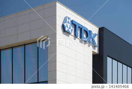 Modern building featuring the TDK logo, sleek architecture with large windows and white panel facade, representing innovation in electronic component manufacturing. Modern building featuring the TDK logo, sleek architecture with large windows and white panel facade, representing innovation in electronic component manufacturing. 141405408