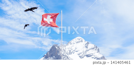 Swiss flag waving against Snow Capped Swiss Alps mountain at Grindelwald First, Switzerland, for Swiss August National Day celebration and holiday. Europe summer hiking trail and travel destination 141405461