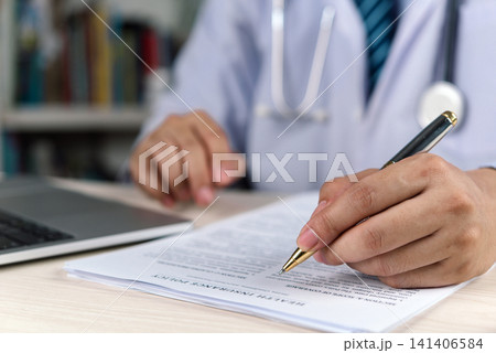Doctor in white coat and stethoscope writing and signing health insurance policy document on desk with laptop. Medical insurance coverage, healthcare paperwork, insurance agreement and policy signing. Doctor in white coat and stethoscope writing and signing health insurance policy document on desk with laptop. Medical insurance coverage, healthcare paperwork, insurance agreement and policy signing. 141406584