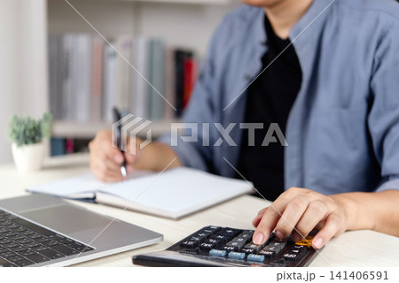 man hands writing in notebook and using calculator with laptop at desk. Personal accounting, home budgeting, small business bookkeeping, freelance finance and tax planning. 141406591
