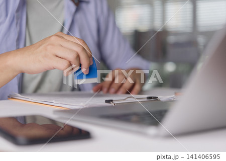 businessman hand pressing rubber stamp on document paperwork with laptop on desk. Concept of business approval, legal contract, agreement, certified validation and compliance. businessman hand pressing rubber stamp on document paperwork with laptop on desk. Concept of business approval, legal contract, agreement, certified validation and compliance. 141406595