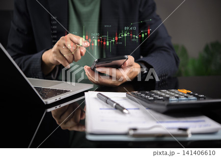 Businessman holding smartphone with digital stock market candlestick chart. Mobile trading concept, financial investment strategy, forex crypto analytics, and accounting with calculator on desk. Businessman holding smartphone with digital stock market candlestick chart. Mobile trading concept, financial investment strategy, forex crypto analytics, and accounting with calculator on desk. 141406610