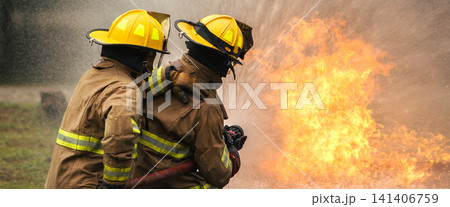 Two firefighters extinguishing a large fire with a hose Two firefighters extinguishing a large fire with a hose 141406759