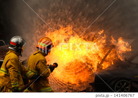 Firefighters extinguishing a burning car with a water hose Firefighters extinguishing a burning car with a water hose 141406767