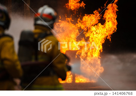 Firefighters tackling a large intense blazing fire outdoors Firefighters tackling a large intense blazing fire outdoors 141406768